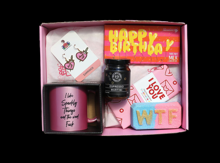 Full image of sweary gift box from Box of Goodies on transparent background. Incudes sweary mug, espresso martini jar, fuck off earrings, birthday chocolate, I love you chocolate and wTF bath bomb in a pink box.